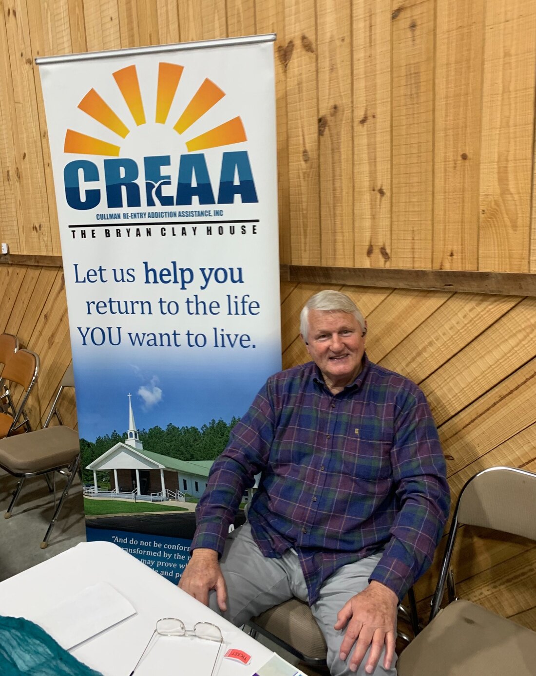Albert Pugh seated beside the CREAA Bryan Clay House banner